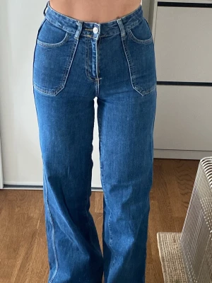 Blåa raka jeans med hög midja - Säljer ett par blå jeans med hög midja och raka ben. Jeansen har klassiska fickor fram och bak, samt en snygg söm längs benen. Tillverkade i denim med en tidlös blå tvätt. Perfekta för en avslappnad och trendig look.