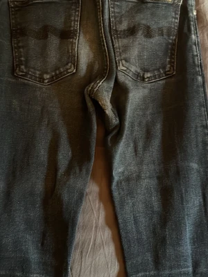 Mörkblå raka jeans med slitningar - Säljer ett par mörkblå nudie jeans. Jeansen har två bakfickor och klassisk femficksdesign. Materialet är denim med en tvättad look som ger en cool och avslappnad stil. Storlek 28W 32L