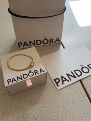 Guldarmband med hjärtlås från Pandora - Snyggt guldfärgat armband från Pandora med ett hjärtformat lås. Armbandet har en elegant och stilren design som passar perfekt till din smyckessamling. Levereras i originalask med Pandora-logga. Storlek  17 