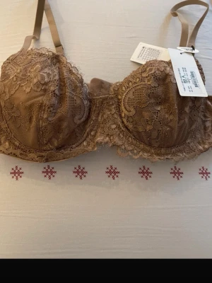 Brun spets-bh med bygel 80A - Snygg bh i brun nyans med vacker spets och bygel för extra stöd. Kuporna är dekorerade med detaljerat spetsmönster och bh:n har justerbara axelband. Perfekt för dig som gillar en feminin och elegant stil.