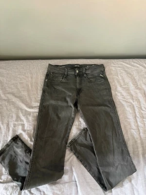 Replay Anbass - Snygga mörkgrå jeans med rak passform och klassisk femficksdesign. Jeansen har normal midja och dragkedjegylf. Materialet ser ut att vara en bomullsblandning med lite stretch för extra komfort. Perfekta till en avslappnad stil.