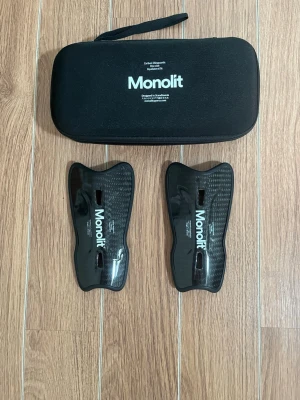 Monolit benskydd  - Säljer ett par svarta benskydd från Monolit . De är lätta, väger endast 30 gram och har en smidig, ergonomisk form. Kommer med ett svart fodral med dragkedja. Perfekta för dig som vill ha skydd utan att tumma på smidigheten.