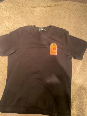 Svart t-shirt från Casablanca - Svart t-shirt från Casablanca Tennis Club med färgglatt tryck på bröstet. Klassisk rund hals och korta ärmar. Tillverkad i mjuk bomull som känns skön mot huden. Perfekt för dig som gillar stilrena plagg med en twist.