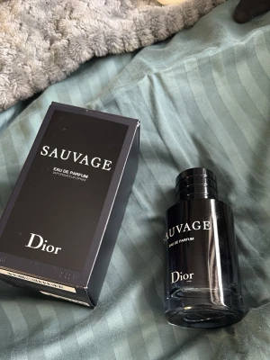 Dior Sauvage Eau de Parfum - Dior Sauvage Eau de Parfum är en ikonisk herrdoft i en elegant, mörk glasflaska med svart lock. Doften har en fräsch och kryddig karaktär och flaskan har en stilren design med vit text. Perfekt för dig som vill ha en modern och maskulin parfym. Ungefär 60% kvar.