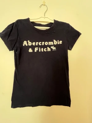 Mörkblå Abercrombie & Fitch t-shirt - Klassisk mörkblå t-shirt från Abercrombie & Fitch med broderad logga i vitt framtill. Den är märkt M men passar bättre för storlek xs-s. Välanvänd men fortfarande i okej skick. 
