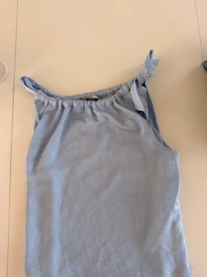 Ljusblå linnetopp med knytband - Söt ljusblå linnetopp med knytband på axlarna och avslappnad passform. Perfekt för varma dagar och enkel att styla med jeans eller kjol. Materialet känns mjukt och luftigt.