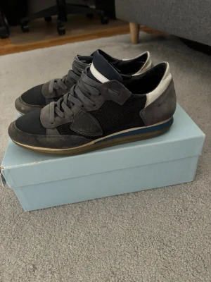 Mörkgrå sneakers med mockadetaljer - Säljer ett par välanvända Phillipe model rockrunners. Skorna är rätt så slitna men har ett tag kvar i sig. Lite slitna på hälen och lite missfärgningar på materialet annars fint. Hör av er vid frågor och funderingar. 