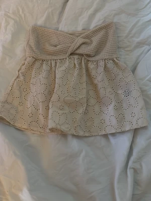 beige topp - Söt beige topp med broderade blommor i spets. toppen har en omlottliknande twist framtill i midjan och ett luftigt, somrigt tyg med stora blommönster. Perfekt för dig som gillar romantisk och bohemisk stil.