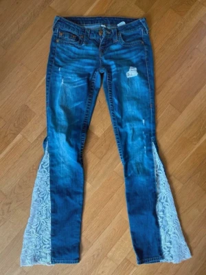 Lowrise flare jeans med SPETS! - Unika blå jeans från True Religion med slitningar och vita spetsinslag längs utsvängda benslut. Klassisk femficksmodell med dekorativa sömmar på bakfickorna och knappgylf. Har sytt dit spetsen själv ⭐️SKRIV FÄRNA VID FRÅGOR ❤️