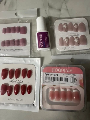 Mixade press-on naglar i rosa & rött - Flera set press-on naglar i olika nyanser av rosa och rött, både glansiga och matta. Ett set har blommönster på ljusrosa bas. Olika former, från mandelformade till fyrkantiga. Inkluderar även ett lim för enkel applicering. Varje grej kostar 75kr. Helt nytt.