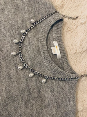 Silverfärgat halsband med pärldroppar - Snyggt halsband i silverfärgad rostfritt med droppformade vita pärlor som hänger längs hela kedjan. Kedjan har en chunky känsla och pärlorna ger en elegant touch. Perfekt för att lyfta vilken outfit som helst med lite extra stil.