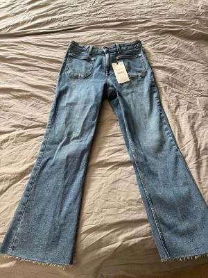 Blå utsvängda jeans med rå kant - Säljer ett par ljusblå jeans med utsvängda ben och rå kant nertill. Jeansen har klassisk femficksmodell och hög midja. Perfekta för dig som gillar en retro och avslappnad stil. Aldrig använda 