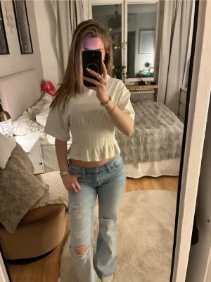 Ljusblå slitna bootcut jeans Gina tricot  - Säljer ett par ljusblå jeans med bootcut-passform och slitningar på båda benen. Jeansen har hög midja och klassisk femficksdesign. Perfekta för en avslappnad och trendig look. Från Gina tricot Young xs 14+