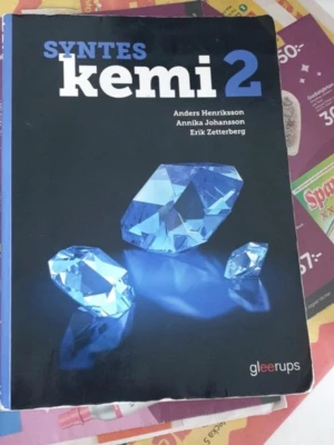 Syntes Kemi 2 kursbok - Kurslitteratur för gymnasiet i kemi, Syntes Kemi 2. Boken har en blå och svart framsida med stora vita och blå bokstäver samt bilder på blå kristaller. Författare: Anders Henriksson, Annika Johansson, Erik Zetterberg. Utgiven av Gleerups.