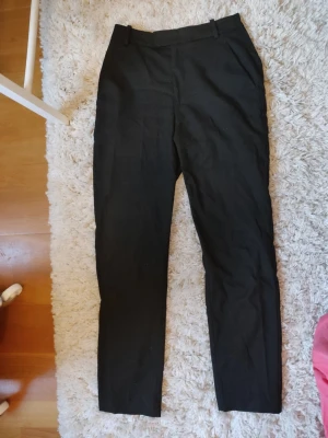 Svarta raka kostymbyxor - Snygga svarta kostymbyxor med raka ben.. Byxorna har bälteshällor och diskreta fickor baktill. Perfekta för en clean och stilren look.