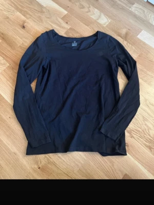 Svart långärmad topp KappAhl - En enkel och stilren svart långärmad topp från KappAhl, tillverkad i mjuk ekologisk bomull. Toppen har rund halsringning och en normal passform, perfekt att matcha med allt i garderoben.