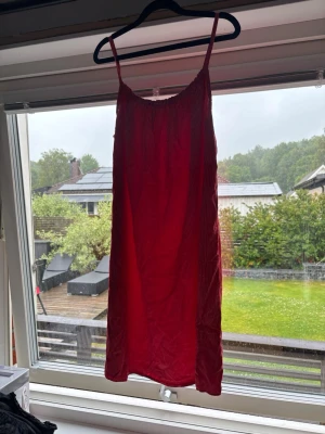 Röd somrig klänning med smala axelband - En röd kortklänning med smala axelband och rak passform. Klänningen har en enkel design och är tillverkad i ett lätt material, perfekt för varma dagar. Passar dig som gillar en avslappnad och stilren look.