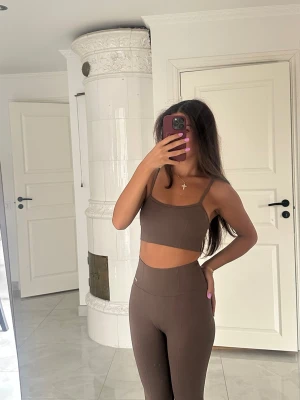 Brunt Aimn set  - Säljer ett brunt Aimn tränings set,  crop top och matchande höga tights. Setet har smala axelband och är tillverkat i ett stretchigt, ribbat material som sitter tight mot kroppen. Perfekt för dig som gillar en enkel och stilren look.