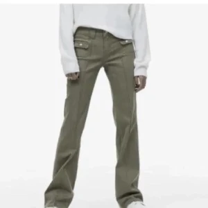 Olivgröna byxor med fickdetaljer - Snygga olivgröna byxor med fickdetaljer framtill. Byxorna har en utsvängd passform och är perfekta för en avslappnad stil. De har en klassisk design med knappar och dragkedja.