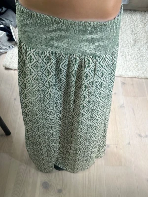 Grön långkjol med mönster - Säljer en grön långkjol med vitt geometriskt mönster och bred smock i midjan. Kjolen är luftig och har en avslappnad passform, perfekt för varma dagar. Materialet känns mjukt och bekvämt mot huden. Strl M men passar perfekt för mig som oftast bär Xs/S då den är väldigt stretchig passar den de flesta