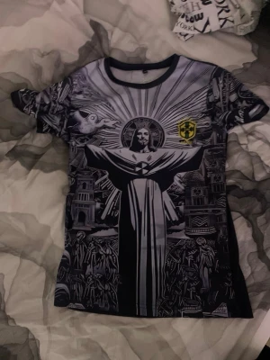 Brasil fotbolls tröja - Unik svart t-shirt med stort tryck av Jesusstatyn och detaljerade motiv på framsidan. T-shirten har korta ärmar och ett gult Brasilien-emblem på bröstet. Baksidan är enfärgad med ett litet Brasilien-tryck upptill.