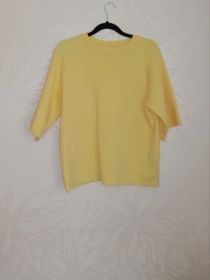 Gul oversized topp med trekvartsärm - En ljusgul oversized topp med trekvartsärm och rund hals. Enkel och stilren design som passar perfekt till jeans eller kjol. Tillverkad i mjukt material för en avslappnad look.