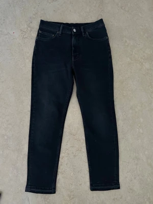Svarta jeans från Acne Studios - Säljer ett par svarta jeans från Acne Studios med klassisk femficksmodell och raka ben. Jeansen har en diskret tvättad look och är tillverkade i ett mjukt bomullsmaterial med lite stretch för extra komfort. Perfekta till en avslappnad stil.