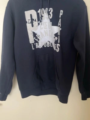 Zandro Studio hoodie - Säljer en svart hoodie med stor vit stjärna och texttryck på framsidan. Hoodien har huva med snöre och en klassisk magficka. Perfekt för en avslappnad streetwear-look.
