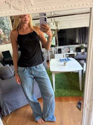 Svart ribbad linnetopp - Säljer en svart ribbad linnetopp med tunna axelband och fin passform. Toppen har en enkel och stilren look som passar perfekt till jeans eller kjol. Materialet känns lätt och luftigt, perfekt för varmare dagar.