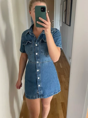 Kort jeansklänning med knappar - Säljer en snygg kort jeansklänning i blå denim. Använd 2 gånger. 
