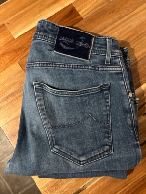 Jacob Cohen 622 - Säljer ett par klassiska blå jeans från Jacob Cohen. Jeansen har raka ben, fem fickor och snygga kontrastsömmar på bakfickorna. Tillverkade i mjukt denimtyg som ger en skön känsla och avslappnad look. Perfekta till en casual outfit.