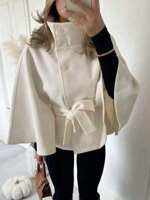 Vit cape-rock med knytband - Stilren vit cape-rock med hög krage, tre stora knappar och brett knytband i midjan. Rocken har vida ärmar och en elegant, minimalistisk look. Perfekt för dig som vill ha en trendig och chic ytterjacka till hösten eller våren.