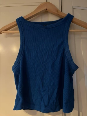 Blå ribbad linnetopp från Bershka - Snygg blå ribbad linnetopp från Bershka. Toppen är ärmlös med breda axelband och har en croppad passform. Perfekt till jeans eller kjol för en trendig. Är lite urtvättad.