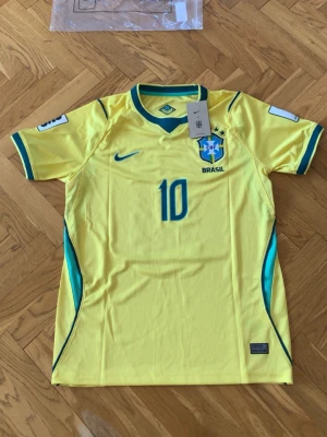 Brasilien Neymar Jr matchtröja gul - Säljer en gul Brasilien matchtröja från Nike med Neymar Jr och nummer 10 på ryggen. Tröjan har blå detaljer, korta ärmar och officiella tryck. Perfekt för dig som älskar fotboll och vill stötta Brasilien på match eller träning.