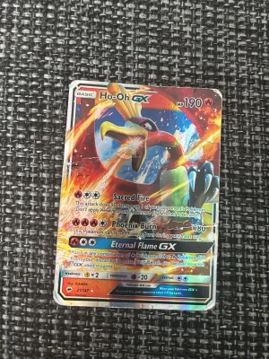 Pokémonkort Ho-Oh GX holografisk - Säljer ett Pokémonkort med Ho-Oh GX motiv. Kortet är holografiskt med färgstark design i rött, gult och blått. Det har 190 HP och flera attacker som Sacred Fire och Phoenix Burn. Perfekt för samlare eller Pokémonfans.