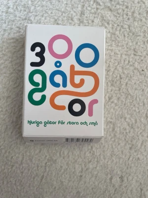 Kortlek 300 gåtor - En kortlek med över 300 kluriga gåtor för både stora och små. Perfekt för att utmana vänner och familj med roliga och knasiga ordvitsar. Färgglad design på vit ask med text i flera färger. Utgiven av Kakao förlag.
