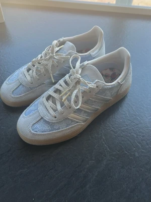 Vita sneakers med silvriga detaljer - Snygga sneakers i vitt med silvriga detaljer och klassisk gummisula. Skorna har ett lågt skaft, mönstrade snören och ovandel i en mix av mocka och textil. Perfekta för dig som vill ha en stilren och trendig look.