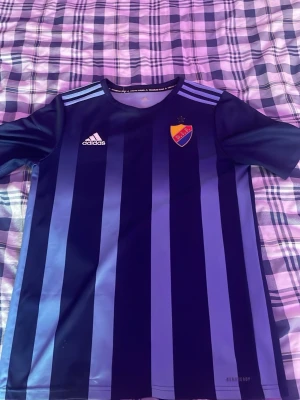 Blårandig Djurgården matchtröja Adidas - Säljer en officiell Djurgården matchtröja från Adidas med blå och mörkblå vertikala ränder. Tröjan har klubbmärke på bröstet, Adidas-logga och nummer 16 med namnet Edvardsen på ryggen. Tillverkad i funktionsmaterial, perfekt för fotboll eller samling. Autograf av Hampus findell och Teo bergvall.    XL i barnstolen 