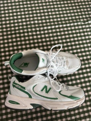 Vita och gröna New Balance 530 - Säljer ett par vita och gröna New Balance 530 sneakers. De är i storlek 44 men SMÅ, passar mer en 43a. Använda 1/2 gånger max pga för små