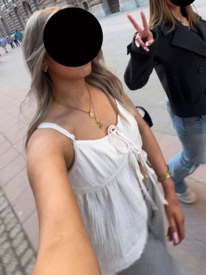 Vit linnetopp med snörning - Säljer en luftig vit linnetopp med tunna virkade axelband och snygg snörning framtill. Toppen har en avslappnad passform och är gjord i ett mjukt, strukturerat tyg som känns perfekt för varma dagar.