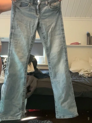Ljusblå raka jeans med fickor - Säljer ett par ljusblå jeans med raka ben och klassiska fem fickor. Jeansen har en snygg tvättad look och silverfärgade knappar. Materialet är denim och passformen är relaxed. Perfekta för en chill och trendig stil.