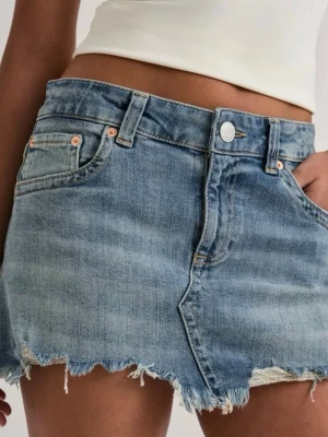 Blå jeanskjol med fransig kant - Säljer en kort blå jeanskjol med rå, fransig kant och klassiska fem fickor. Kjolen har en avslappnad passform och stängs med knapp och dragkedja framtill. Perfekt för dig som gillar en casual och trendig stil. Aldrig använd! 