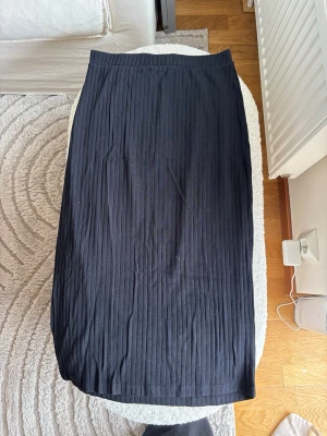 Svart ribbad kjol från Even&Odd - Säljer en svart kjol från Even&Odd med ribbad struktur. Kjolen har en rak passform och är gjord i ett mjukt, stretchigt material som sitter bekvämt i midjan. Perfekt att styla med sneakers eller boots för en clean look.