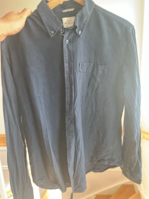 Mörkblå skjorta från Ben Sherman - Säljer en klassisk mörkblå skjorta från Ben Sherman i storlek M. Skjortan har knappar hela vägen, bröstficka och button-down krage. Tillverkad i mjuk bomull och passar perfekt till en avslappnad men stilren look. Säljer då jag har vuxit ur den. Hör gärna av er vid frågor!