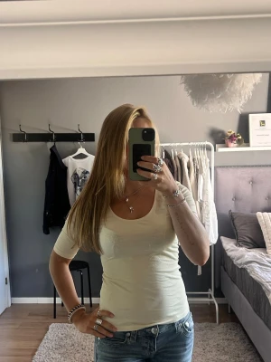 Beige t-shirt med rund hals - En enkel och stilren beige t-shirt med rundad, djup urringning och halvlånga ärmar. T-shirten har en smickrande passform och är tillverkad i ett mjukt, stretchigt material som sitter bekvämt på kroppen. Perfekt till jeans eller kjol för en clean look.