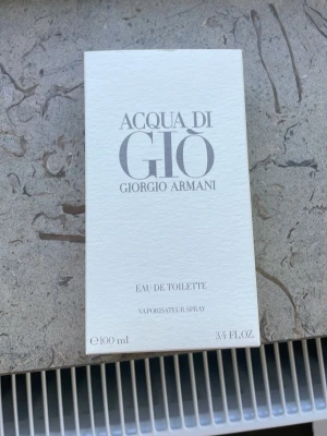 Acqua di Giò Eau de Toilette 100 ml - Acqua di Giò från Giorgio Armani är en parfym i en frostad glasflaska med stilren design och silverfärgad kork. Flaskan rymmer 100 ml och har en modern, minimalistisk look. Förpackningen är ljus med tydlig logga och text i grått.