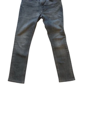 Nudie jeans - Säljer ett par mörkgrå jeans med rak passform och klassisk femficksdesign. Jeansen har normal midja och är tillverkade i denim med lätt tvättad look. Perfekta för en avslappnad och stilren outfit.