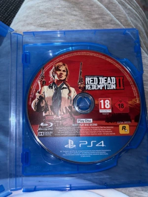 Red Dead Redemption II till PS4 - Red Dead Redemption II till PlayStation 4, två Blu-ray-skivor i originalfodral. Omslagen är röda med karaktärer från spelet och tydlig 18-årsgräns. Perfekt för dig som gillar action, äventyr och vilda västern-tema.