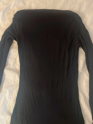 Intimissimi Svart långärmad T-shirt  - Intimissimi svart, långärmad topp med offshoulder-design. Tunn och stretchig modell som sitter tight mot kroppen. Perfekt att styla med jeans eller kjol för en trendig look.