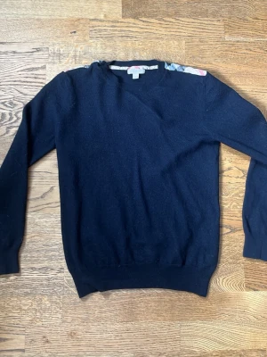 Mörkblå stickad tröja från Burberry - Snygg mörkblå stickad tröja från Burberry med rund halsringning och diskreta ribbade muddar vid ärmslut och nederkant. Tillverkad i mjukt material som känns lyxigt och passar perfekt till lager på lager. Klassisk och stilren design. BARN STORLEK!